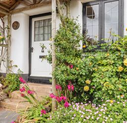 The entrance to a cottage with a white door black framed windows and flowers in the garden at Rose Cottage in Holcombe in Teignmouth