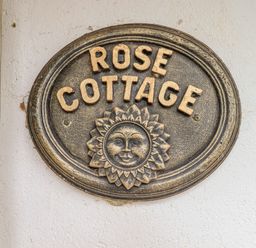 A wall plaque with the words Rose Cottage and a sun face decoration at Rose Cottage in Holcombe Teignmouth