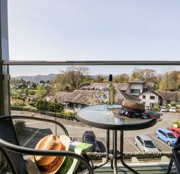 A balcony with a round table holding a bottle of white wine two wine glasses a hat and sunglasses overlooking buildings and parked cars at Claife Heights in Windermere
