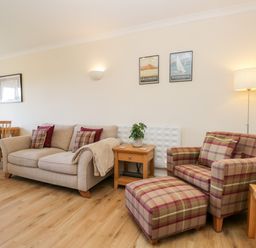 A living room with a beige sofa and a plaid armchair with matching footstool at Claife Heights in Windermere