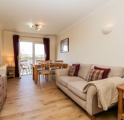 A living room with a beige sofa and wooden dining table near a sliding glass door at Claife Heights in Windermere