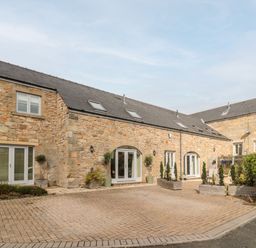Exterior view of a stone building with multiple white doors and windows and potted plants at Calm Skies in Scremerston near Berwick-Upon-Tweed
