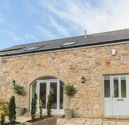 Exterior view of a stone building with arched glass doors a front door and potted plants at Calm Skies in Scremerston near Berwick-Upon-Tweed