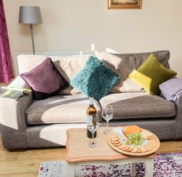 A living room with a beige sofa and colorful cushions a small wooden coffee table with wine and snacks at Healey Farm Cottage Rothbury