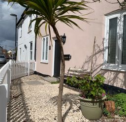 The front garden of a house with a white picket fence a potted plant a small tree and a bench outside the door at Smugglers Cottage Christchurch