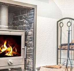 A wood burning stove with fire inside and a black metal firewood rack with firewood at Smugglers Cottage in Christchurch