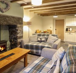 A living room with sofas covered in plaid blankets a wooden coffee table and a fireplace next to a kitchen and dining area at Bwthyn Y Bugail in Manod near Blaenau Ffestiniog