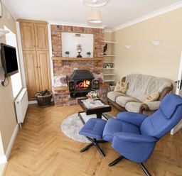 A living room with a blue recliner chair a sofa a brick fireplace and a wall-mounted television at The Water's Edge in Boyle County Roscommon