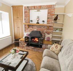 A living room with a brick fireplace a wood-burning stove a beige sofa and a coffee table with flowers at The Waters Edge in Boyle County Roscommon