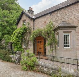 The exterior of a stone house with a wooden door and climbing plants at The Lodge in Greystoke