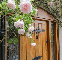 A wooden door with decorative black hardware surrounded by climbing pink roses and stone walls at The Lodge in Greystoke