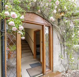 An open wooden front door with glass panes showing a staircase inside and climbing roses around the doorway at The Lodge in Greystoke