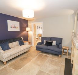 A living room with two sofas a floor lamp a fireplace and a wall clock at Dazie Cottage in Broadway