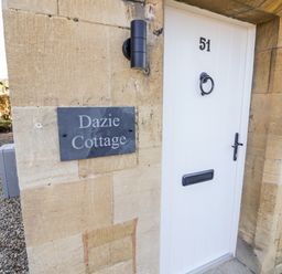 A white door with number 51 and a sign reading Dazie Cottage on a stone wall at Dazie Cottage in Broadway