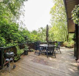 An outdoor wooden deck with a table and chairs surrounded by green trees at Scafell Lodge Skiptory Howe 7 White Cross Bay Holiday Park near Windermere