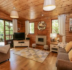 A wooden living room with a television sofa two stools a rug lamps and windows at Scafell Lodge in Skiptory Howe 7 White Cross Bay Holiday Park near Windermere