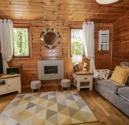 A living room with wooden walls a gray sofa yellow cushions a patterned rug and a TV on a cabinet at Scafell Lodge Skiptory Howe 7 White Cross Bay Holiday Park near Windermere