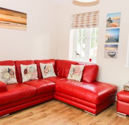A living room with a red leather sectional sofa and marine-themed cushions at Meadow View in Filey