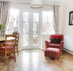 A dining area with wooden table and chairs a red striped armchair with matching footstool and a large window at Meadow View in Filey