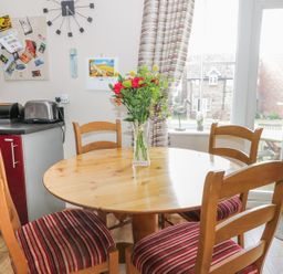 A dining area with a round wooden table and four chairs with striped cushions and a vase with flowers at Meadow View in Filey