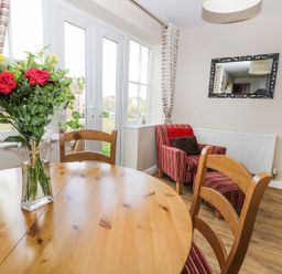 A dining area with a wooden table and chairs a vase with flowers a striped armchair and a wall mirror at Meadow View in Filey