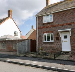 A street view of brick and white houses with a white front door and fenced front garden at The Beach House in West Bay