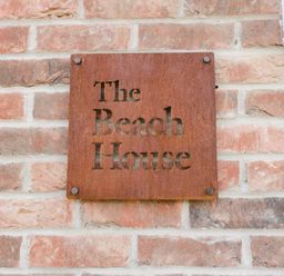 A rusted metal sign with The Beach House text mounted on a brick wall at The Beach House in West Bay