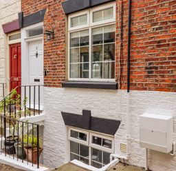 A brick and white painted building exterior with two doors and two windows with plants in pots near stairs at Anchor Cottage in Whitby