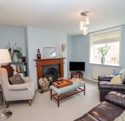 A living room with a fireplace a beige armchair a brown leather sofa a coffee table and a window at Anchor Cottage in Whitby