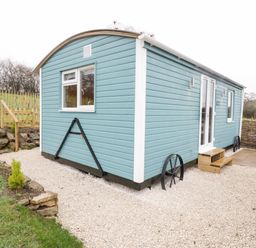 A light blue tiny house on wheels with white trim on a gravel area near a small wooden fence at Robins Nest in Napton-On-The-Hill