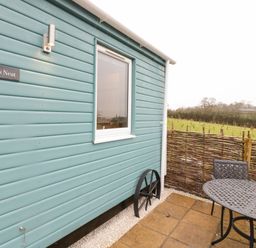 Exterior view of a blue wooden building with a window and metal patio furniture next to a wicker fence at Robins Nest in Napton-On-The-Hill