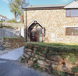 The exterior of a stone cottage with a paved walkway and stone retaining walls at Brewers Cottage in Looe