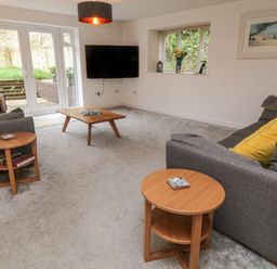 A living room with two gray sofas yellow cushions wooden coffee tables wall-mounted TV and large glass doors at Brewers Cottage in Looe