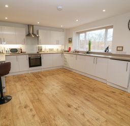 A kitchen with white cabinets wooden floor a bar stool and a large window at Brewers Cottage in Looe