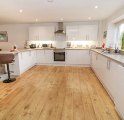 A kitchen with white cabinets wooden floor a stove microwave sink and bar stools at Brewers Cottage in Looe