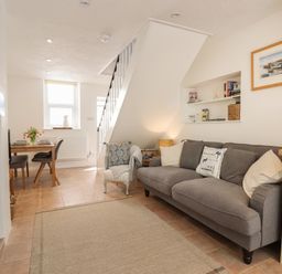 A living room with a gray sofa a small armchair a dining table with chairs and a staircase at Quayside Cottage in Teignmouth