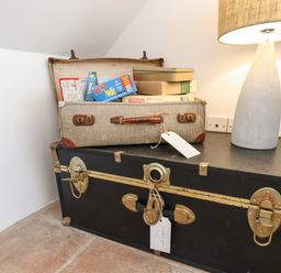 An open vintage suitcase with board games on top of a black trunk next to a lamp in a corner of a room at Quayside Cottage in Teignmouth