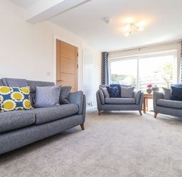 A living room with three grey sofas cushions a wooden door and large window with curtains at Pickney House in Killigarth near Polperro