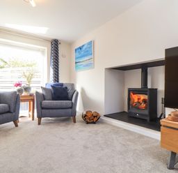 A living room with gray armchairs a fireplace with burning logs and a television at Pickney House in Killigarth near Polperro
