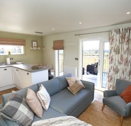 A living room with a blue sofa and armchair next to a kitchen and patio doors at The Swift in Wem