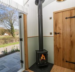A corner with a wood burning stove and a wooden door next to an open door showing an outside view at Acorn in Bleadon