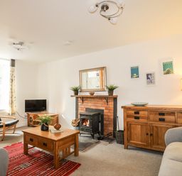 A living room with a fireplace, wooden furniture, a television, armchair, and a red rug at 9 Ty Du Road in Llanberis