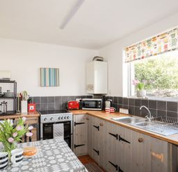 A kitchen with wooden countertops a dual sink a stove a microwave a toaster a kettle mugs flowers and a table with tulips and cups at 9 Ty Du Road in Llanberis