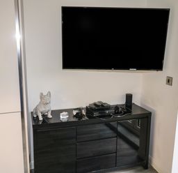 A wall-mounted television above a black cabinet with gaming console and decorative items at Sunnydene in Paignton