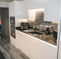 A kitchen with white cabinets black countertop black appliances and a gray tiled backsplash at Sunnydene in Paignton