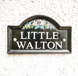 A black sign with flowers reading Little Walton on a white textured wall at Little Walton in Burnham-On-Sea
