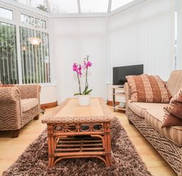 A conservatory with wicker sofas a wooden coffee table with a plant and a television on a stand at Little Walton in Burnham-On-Sea