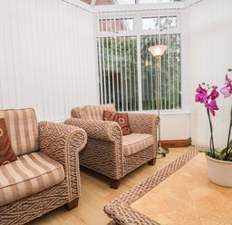 A seating area with two woven armchairs with striped cushions and a potted orchid on a table at Little Walton in Burnham-On-Sea