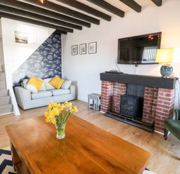 A living room with a wooden coffee table and a vase of yellow flowers at Malltraeth Cottage in Malltraeth