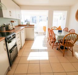 A kitchen with white cabinets wooden countertops a black stove and a dining table with six wooden chairs at Malltraeth Cottage in Malltraeth